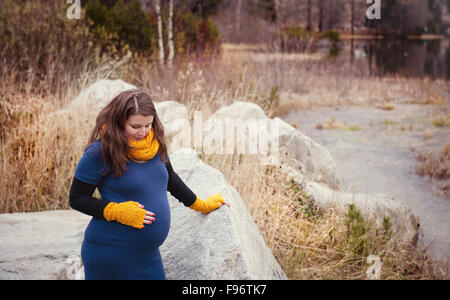 Schöne Outdoor-schwangere Frau Porträt in der herbstlichen Natur, steht Frau auf Felsen Stockfoto