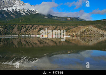 Ein Canadian National Güterzug vorbei entlang der Uferlinie des Jasper Lake im Jasper National Park in Alberta, Kanada Stockfoto