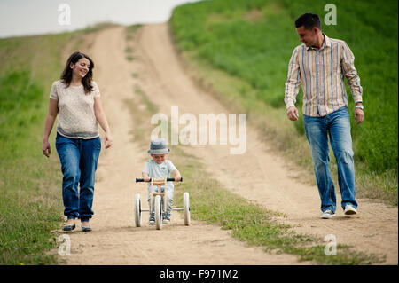 Glückliche Familie mit kleinen Jungen auf hölzernen Dreirad Wandern in ntaure Stockfoto