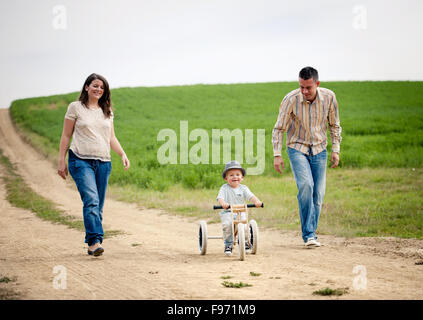 Glückliche Familie mit kleinen Jungen auf hölzernen Dreirad Wandern in ntaure Stockfoto