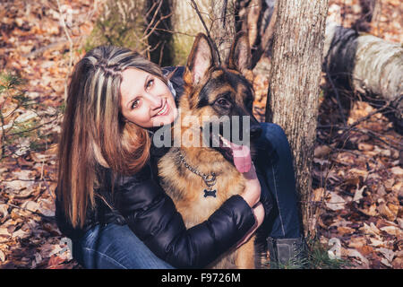 Junge Frau lächelnd mit einem Deutscher Schäferhund im Freien im Wald Stockfoto