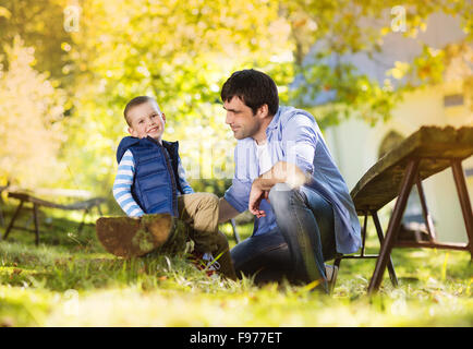 Vater und Sohn gemeinsam Zeit zu verbringen, im Sommer Natur, ist kleiner Junge seinem Vater Schuhe binden. Stockfoto