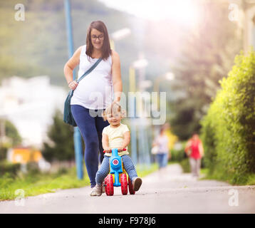 Junge schwangere Mutter mit ihrer kleinen Tochter auf kleine Motorrad Zeit miteinander zu verbringen, im park