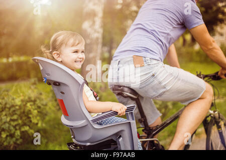 Junger Vater mit seiner kleinen Tochter mit dem Fahrrad in sonnigen, grünen park Stockfoto