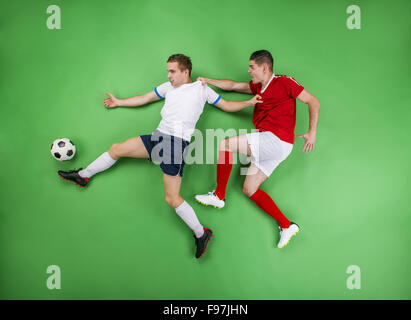Zwei begeisterte Fußballer kämpfen für einen Ball. Studio auf einem grünen Hintergrund gedreht.
