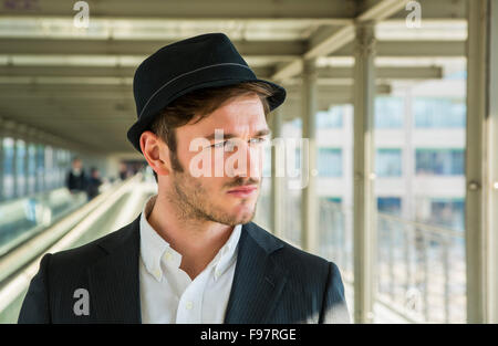 Kopf und Schultern Porträt Stylist junger Mann tragen Anzug und Hut Blick zur Seite aus Fenster stehen auf beweglichen Si Stockfoto