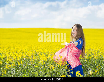 Fröhliches junges Mädchen im blauen Kleid und roten Schal in gelben Raps Feld Freizeit genießen Stockfoto