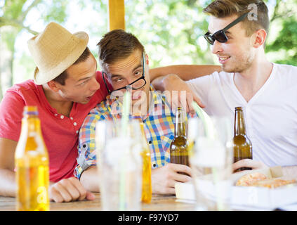 Drei glückliche Freunde Bier trinken, plaudern und Spaß im Gastgarten Stockfoto