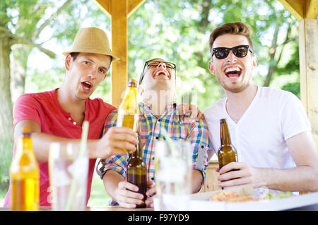 Drei glückliche Freunde Bier trinken, plaudern und Spaß im Gastgarten Stockfoto