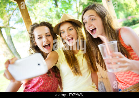 Drei schöne Mädchen trinken und nehmen Selfie mit Smartphone im Gastgarten Stockfoto