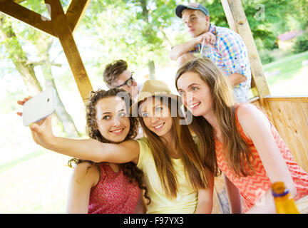 Drei schöne Mädchen trinken und nehmen Selfie mit Smartphone im Gastgarten Stockfoto