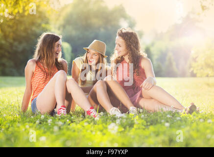Drei schöne Mädchen gemeinsam lachen und sitzen auf dem Rasen im Freien in einem Park. Stockfoto