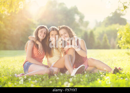 Drei schöne Mädchen gemeinsam lachen und sitzen auf dem Rasen im Freien in einem Park. Stockfoto