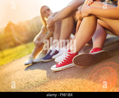 Beine und Sneakers von Teenager-Jungen und Mädchen sitzen auf dem Bürgersteig Stockfoto