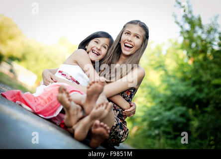 Zwei Schwestern Lachen und umarmt auf Bürgersteig in sonnigen, grünen park Stockfoto