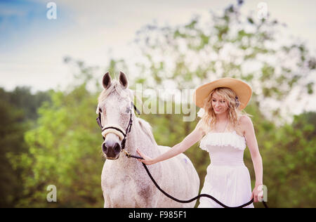 Frau im weißen Kleid mit Pferd in der grünen Landschaft wandern Stockfoto