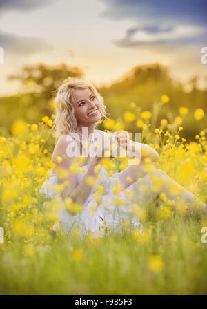 Mädchen sitzen zwischen gelben Blumen auf sonnigen Tag Stockfoto