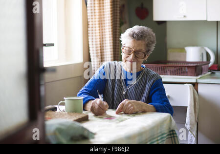 Alte Frau sitzt in ihrer Landhausküche Stockfoto