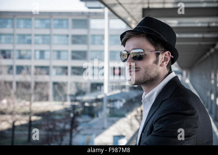 Kopf und Schultern Porträt Stylist junger Mann tragen Anzug und Hut Blick zur Seite aus Fenster stehen auf beweglichen Si Stockfoto