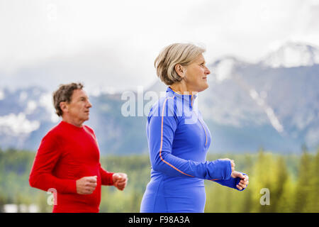 Älteres paar jogging Runde Tarn in wunderschöne Berge, Hügel und Hotel im Hintergrund Stockfoto