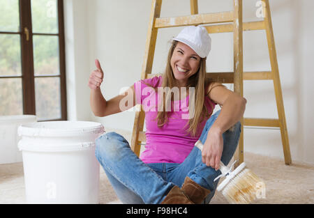 Glücklich lächelnde Frau auf dem Boden sitzend und mit einer Pause von der Malerei Stockfoto