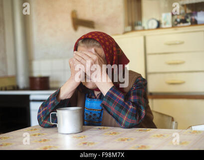 Sehr alte traurige Frau im Kopftuch sitzt in ihrer Küche countrystyle Stockfoto