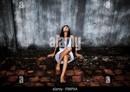 Eine junge asiatische Frau in einem weißen Slip sitzt und starrt sie auf eine industrielle Dach in Hanoi, Vietnam. Stockfoto