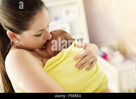 Junge Mutter halten und küssen ihr neugeborenes Mädchen zu Hause Stockfoto