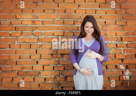 Outdoor Portrait schöne schwangere Frau hält ihren Bauch, die Mauer im Hintergrund Stockfoto