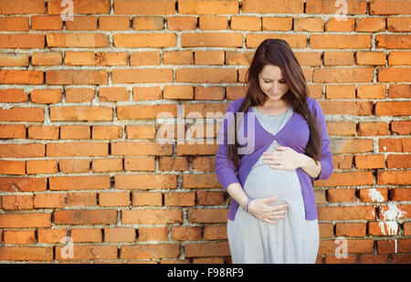 Outdoor Portrait schöne schwangere Frau hält ihren Bauch, die Mauer im Hintergrund Stockfoto