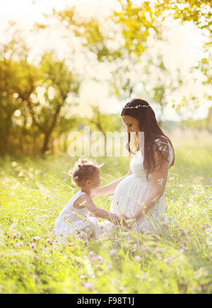 Niedliche kleine Mädchen berühren schwangeren Bauch der Mutter in der Sommer-Natur Stockfoto