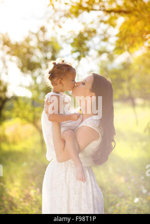 Glückliche junge schwangere Mutter und ihre kleine Tochter küssen im Sommer-Natur Stockfoto