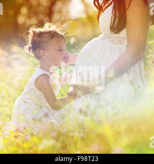 Niedliche kleine Mädchen berühren schwangeren Bauch der Mutter in der Sommer-Natur Stockfoto