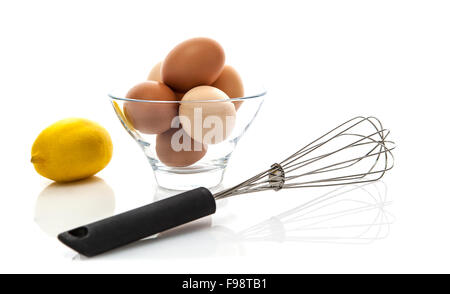 Metall-Schneebesen mit frischen Eiern und Zitrone auf weißem Hintergrund Stockfoto