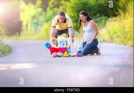 Kleines Mädchen gefallen an ihr Fahrrad, ihre Eltern helfen ihr aufzustehen Stockfoto