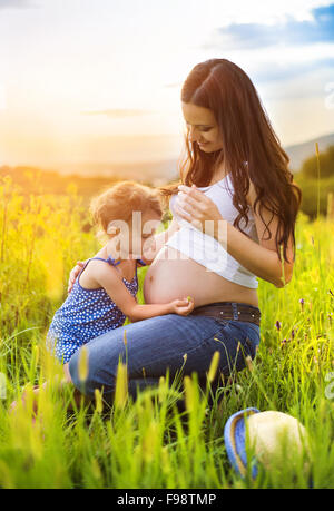 Niedliche kleine Mädchen berühren schwangeren Bauch der Mutter in der Sommer-Natur Stockfoto
