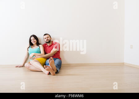 Junges Paar sitzt auf dem Boden in ihren leeren neuen Haus. Frau ist schwanger. Stockfoto