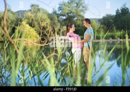 Glückliche junge schwangere paar umarmt am See Stockfoto