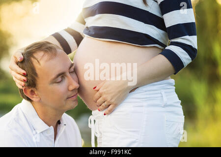 Mann hört Bauch der schwangeren Frau in der Natur Stockfoto