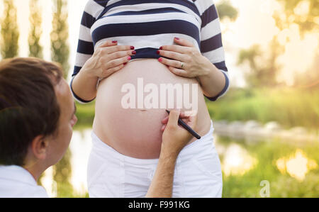 Man schreibt einen Namen auf Bauch der schwangeren Frau in der Natur Stockfoto