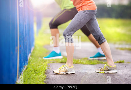 Junges Paar stretching nach dem Lauf auf Asphalt bei Regenwetter. Details der Beine. Stockfoto