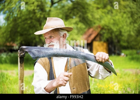 Alter Bauer mit Bart seine Sense schärfen, vor der Verwendung zu traditionell mähen den Rasen Stockfoto