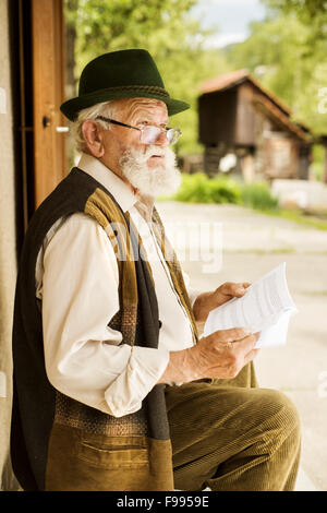 Alter Mann liest Zeitung vor seinem Haus Stockfoto