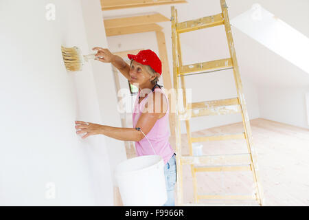 Ältere Frau Malerei Wand im neuen Haus. Sie nutzt Leiter. Stockfoto