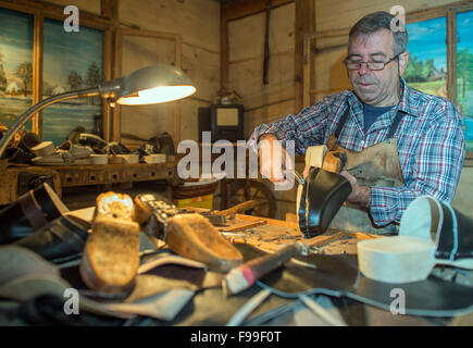 Clog-Hersteller Manfred Karolczak deckt einen Schuh mit Leder an seinem Arbeitsplatz in der Spreewald-Gemeinde Burg (Brandenburg), Deutschland, 07. Dezember 2015. Seit 1909 haben in dem kleinen Familienbetrieb handgefertigten Holzschuhe aus Pappel und Erle Holz geschnitzt worden. Die Holzplatte ist mit Schweinsleder überzogen und mit Draht geklemmt. Nach etwa einer Stunde ein Paar Holzschuhe gemacht. Die Schuhe eignen sich besonders für den Garten und sind relativ unempfindlich gegenüber Feuchtigkeit aufgrund der Naturmaterialien. Foto: Patrick Pleul/dpa Stockfoto