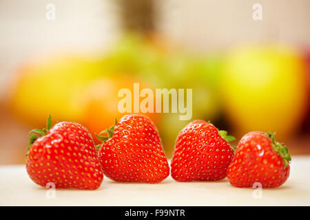 Vier rote Erdbeeren mit anderen Früchten in einer Küche Stockfoto