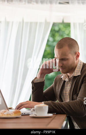 Business-Mann telefonieren mit einem Handy und arbeitet an seinem Laptop im Straßencafé Stockfoto