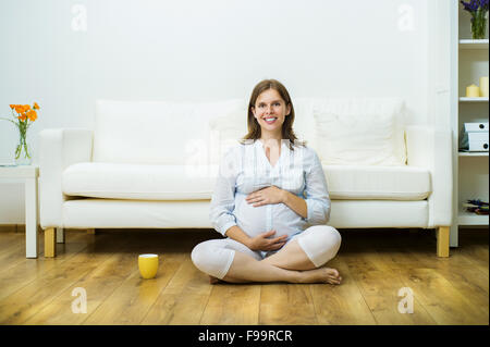 Porträt von glücklich schwangere Frau sitzen auf dem Boden durch das Sofa, isoliert auf weißem Hintergrund Stockfoto