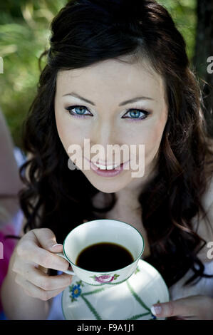 Braut im weißen Hochzeitskleid Kaffeetrinken auf der Wiese Stockfoto