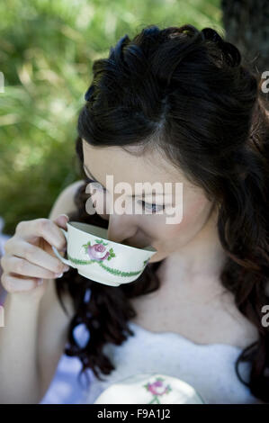 Braut im weißen Hochzeitskleid Kaffeetrinken auf der Wiese Stockfoto